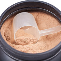 Scoop of chocolate whey isolate protein in a black plastick cont